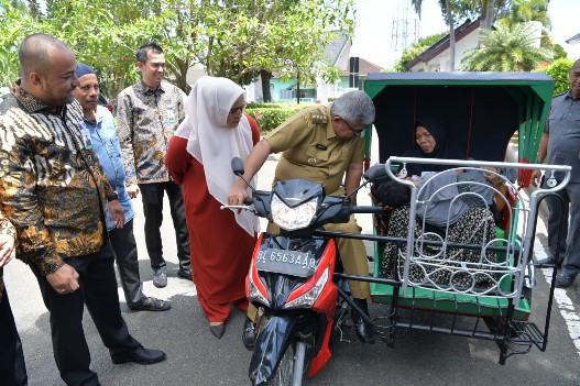 Pj Gubernur Aceh Bustami Hamzah bersama istri Mellani Subarni, didampingi Plt Dirut Bank Aceh Syariah Fadhil Ilyas, menyerahkan bantuan satu unit becak untuk Abdul Azis untuk operasional pengobatan anaknya Muhammad Ramadhan yang menderita sakit lumpuh sejak lahir, di halaman Pendopo Gubernur, Senin (10/6/2024). Foto: Istimewa