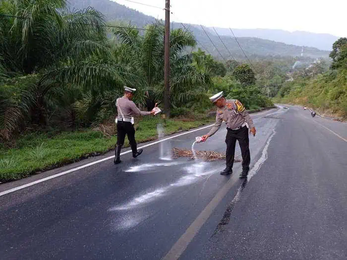 Polisi membersihkan tumpahan CPO yang menggenangi ruas jalan nasional Tapaktuan—Subulussalam, di Gunung Kapur, Trumon Tengah, Aceh Selatan, pada Selasa, 23 Juli 2204. (Foto: Ditlantas Polda Aceh)