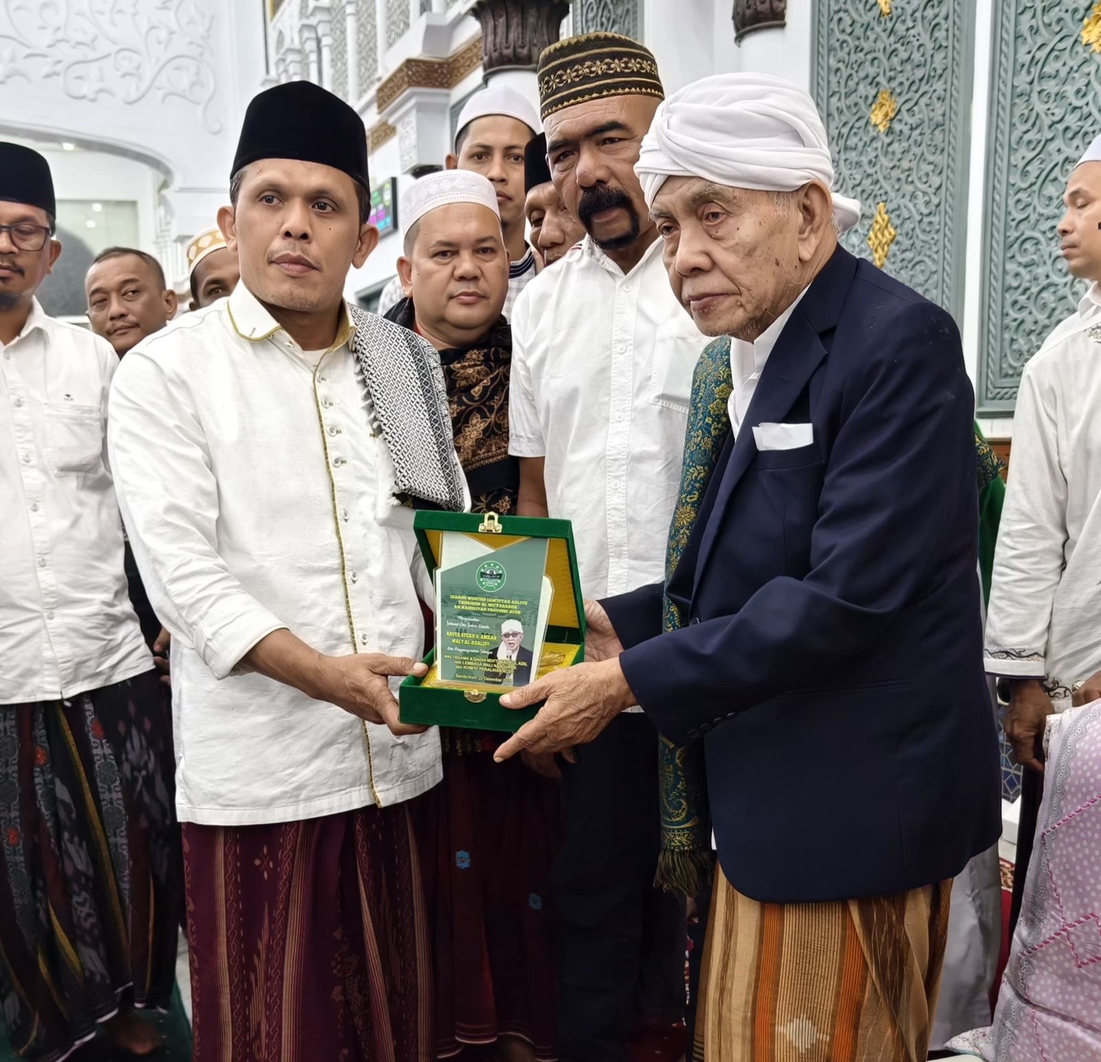 Ketua JATMAN Provinsi Aceh Tgk H Syukri Daud Pango menyerahkan plakat ucapan selamat kepada Abuya Syeikh H Amran Waly Al-Khalidy sebagai Wali Agama Aceh di Masjid Raya Baiturrahman Banda Aceh, Ahad malam (22/12). (Foto: Dok. Infoaceh.net)